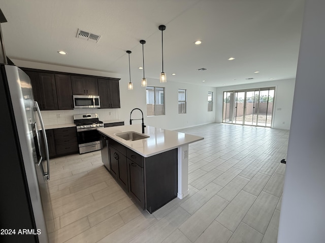 kitchen with sink, hanging light fixtures, stainless steel appliances, decorative backsplash, and a center island with sink