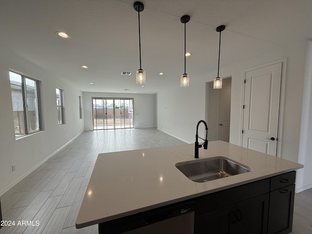 kitchen with dishwasher, a kitchen island with sink, sink, decorative light fixtures, and light stone counters