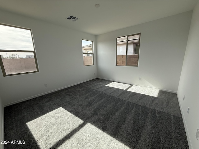 spare room with a wealth of natural light and dark carpet