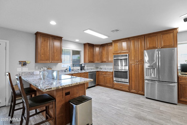 kitchen featuring visible vents, a peninsula, brown cabinets, a sink, and stainless steel appliances