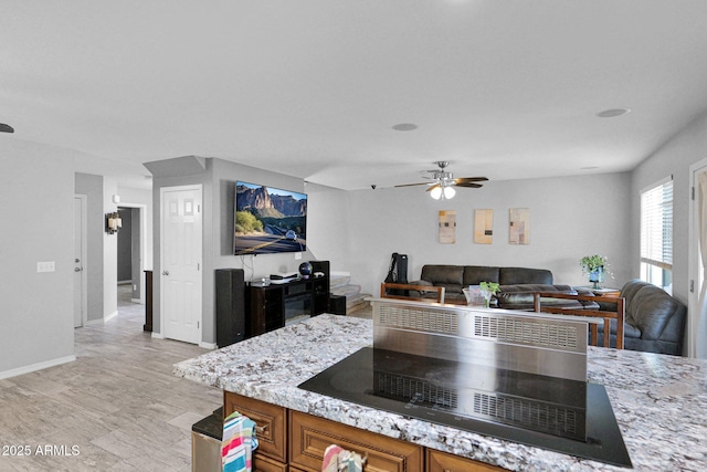 kitchen featuring brown cabinets, light stone countertops, black electric stovetop, a ceiling fan, and baseboards