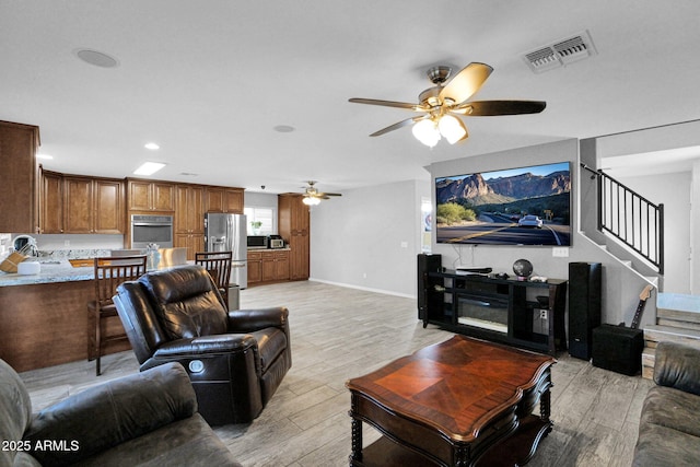 living room featuring visible vents, baseboards, ceiling fan, stairway, and light wood-type flooring