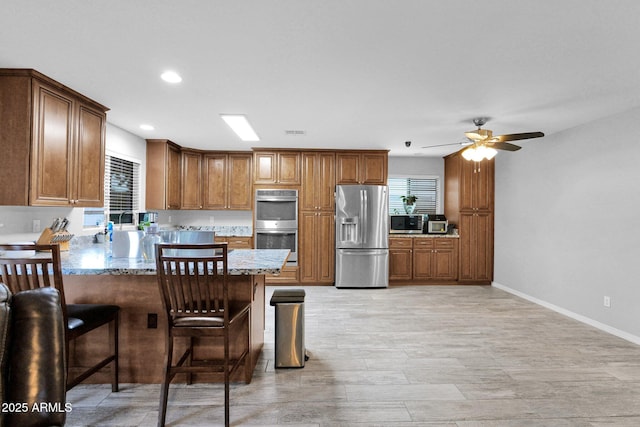 kitchen with light stone counters, stainless steel appliances, a ceiling fan, recessed lighting, and a peninsula