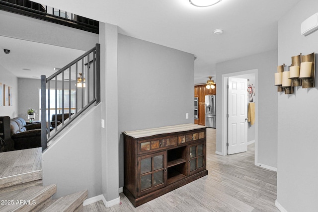 interior space with light wood-type flooring, stairs, a wall unit AC, and baseboards