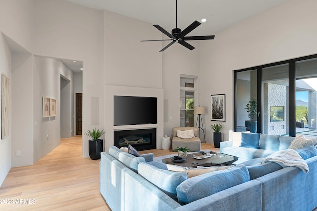 living room with ceiling fan, a wealth of natural light, light hardwood / wood-style floors, and a towering ceiling