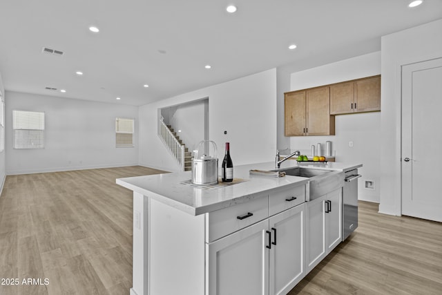 kitchen with light stone countertops, visible vents, recessed lighting, a kitchen island with sink, and light wood-style floors