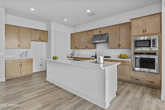 kitchen with under cabinet range hood, light countertops, appliances with stainless steel finishes, light wood-style floors, and a sink