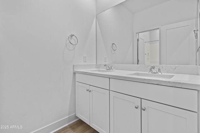 bathroom with double vanity, wood finished floors, baseboards, and a sink