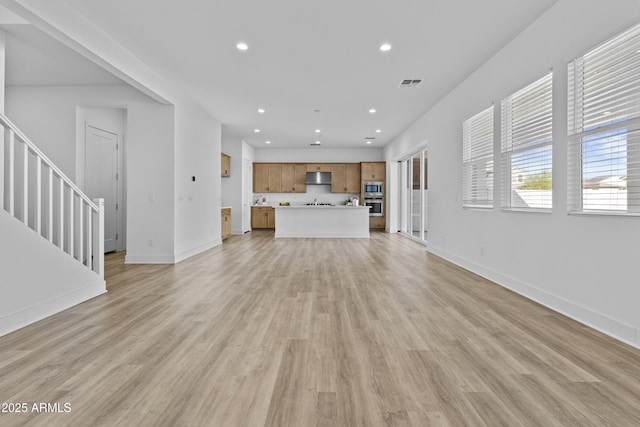 unfurnished living room with visible vents, light wood finished floors, baseboards, recessed lighting, and stairs