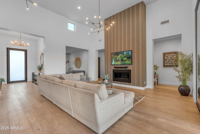 living area with baseboards, visible vents, light wood-type flooring, a chandelier, and a large fireplace