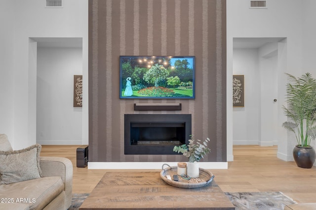 living area with visible vents, wood finished floors, baseboards, and a large fireplace