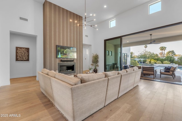 living area featuring a notable chandelier, light wood-style flooring, a fireplace, and a high ceiling