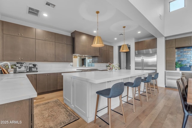 kitchen with visible vents, light wood finished floors, premium range hood, a sink, and a kitchen breakfast bar