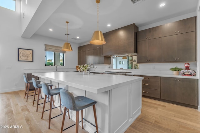 kitchen with custom exhaust hood, stainless steel gas stovetop, light wood-style flooring, and light countertops