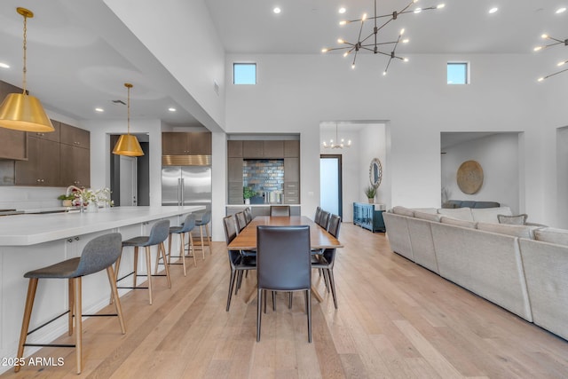 dining room with recessed lighting, light wood-style floors, a towering ceiling, and a chandelier