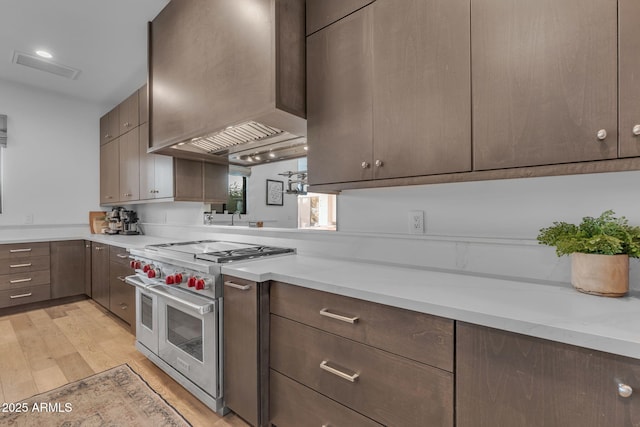 kitchen with dark brown cabinets, double oven range, light countertops, light wood-style flooring, and custom exhaust hood