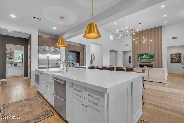 kitchen featuring visible vents, a center island with sink, built in fridge, light wood-style floors, and light countertops