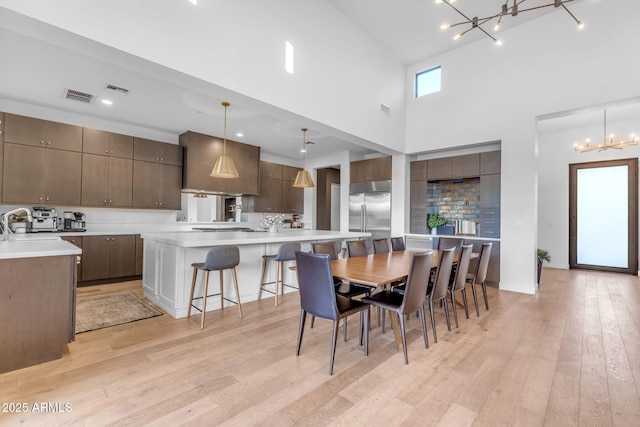 dining space featuring a notable chandelier, visible vents, light wood-style flooring, and a high ceiling