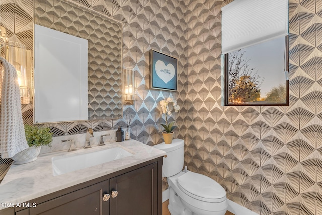 bathroom with toilet, vanity, and wallpapered walls