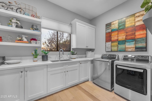 laundry area featuring cabinet space, washing machine and dryer, light wood-type flooring, and a sink