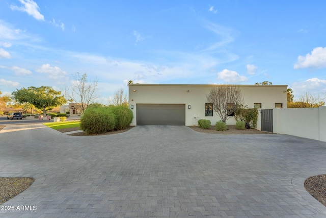 view of front facade with a garage, decorative driveway, fence, and stucco siding