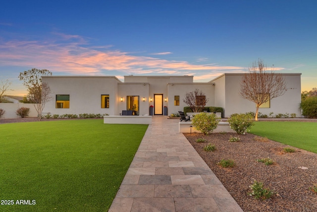 back of house at dusk with a patio area, a lawn, and stucco siding