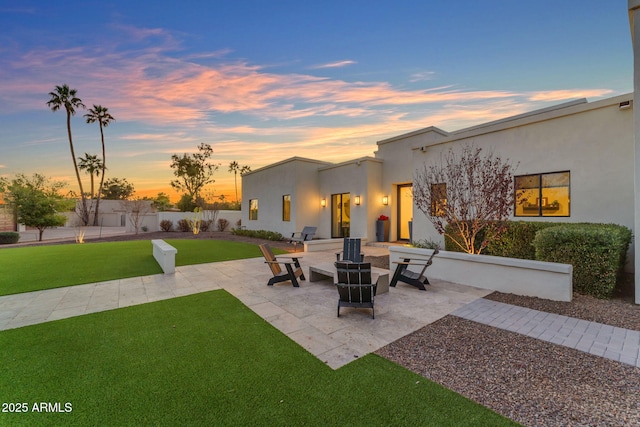 patio terrace at dusk featuring a lawn and fence