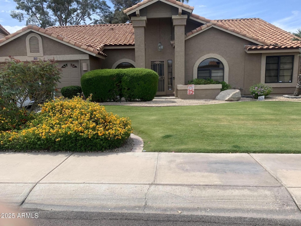 mediterranean / spanish-style home with stucco siding, a tiled roof, a front yard, and a garage