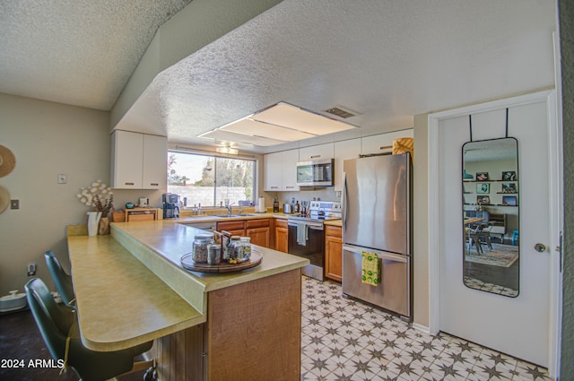 kitchen featuring sink, a textured ceiling, kitchen peninsula, white cabinetry, and stainless steel appliances