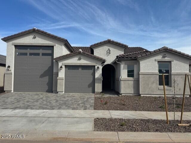 mediterranean / spanish-style home with stucco siding, driveway, a garage, and a tile roof