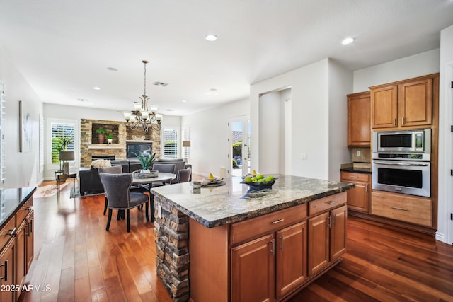 2207 W Hidden Treasure Way, Phoenix, AZ 85086 - kitchen with appliances with stainless steel finishes, dark wood-type flooring, brown cabinetry, a stone fireplace, and a center island