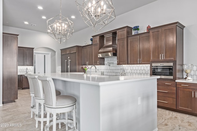 kitchen with decorative light fixtures, custom exhaust hood, stainless steel oven, tasteful backsplash, and a breakfast bar area