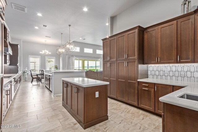 kitchen with pendant lighting, light tile floors, a kitchen island, a chandelier, and backsplash