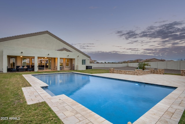 pool at dusk with a lawn and a patio area