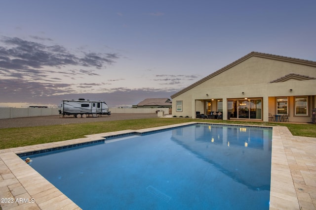 pool at dusk with a patio area and a yard