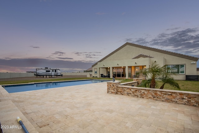 pool at dusk featuring a lawn and a patio area