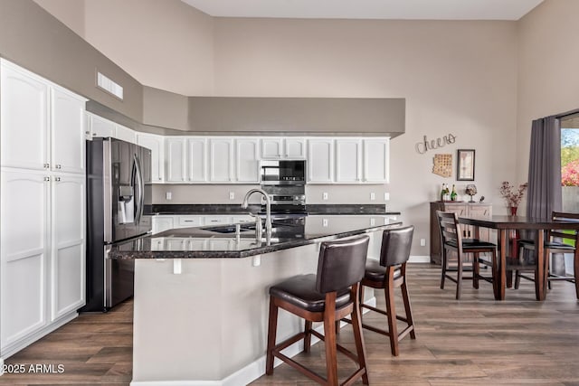 kitchen featuring a kitchen bar, a high ceiling, white cabinetry, and appliances with stainless steel finishes