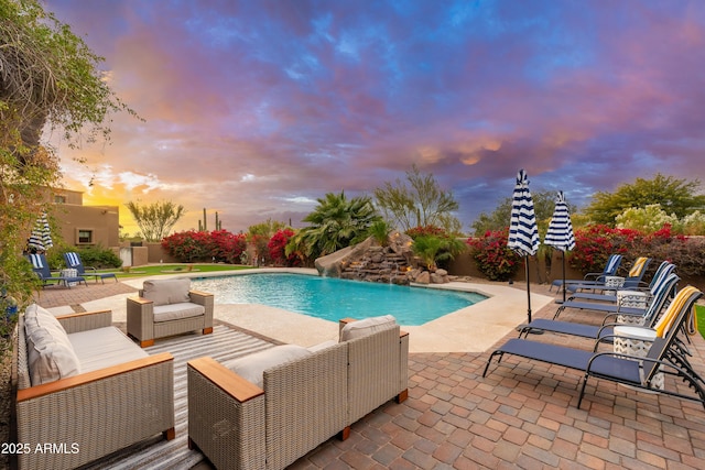 pool at dusk with pool water feature, outdoor lounge area, and a patio