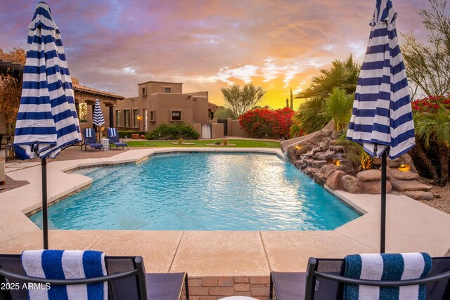 pool at dusk featuring pool water feature and a patio