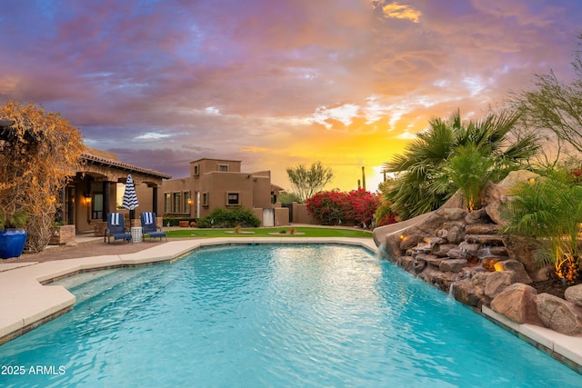 pool at dusk featuring pool water feature and a patio area