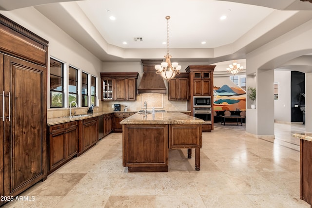 kitchen featuring premium range hood, an inviting chandelier, hanging light fixtures, black microwave, and an island with sink