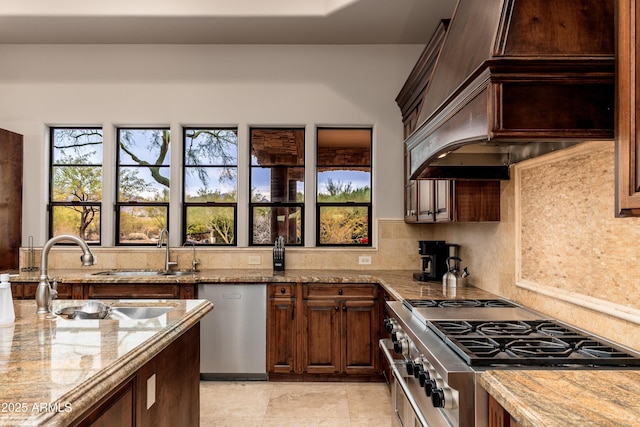 kitchen with premium range hood, sink, decorative backsplash, light stone counters, and stainless steel appliances