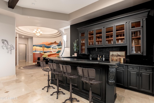 bar featuring a tray ceiling, a chandelier, and decorative backsplash