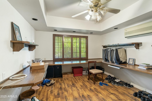 interior space with an AC wall unit, built in desk, hardwood / wood-style flooring, ceiling fan, and a raised ceiling