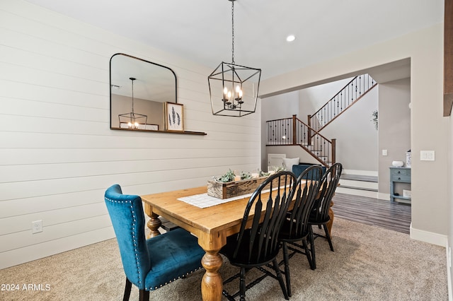 dining area featuring carpet flooring, a chandelier, and wood walls