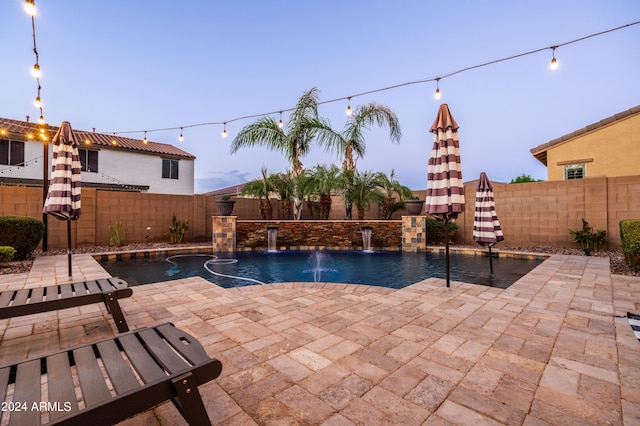 pool at dusk featuring pool water feature and a patio