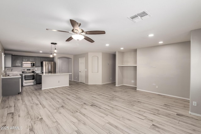 unfurnished living room with arched walkways, visible vents, a sink, ceiling fan, and light wood-type flooring