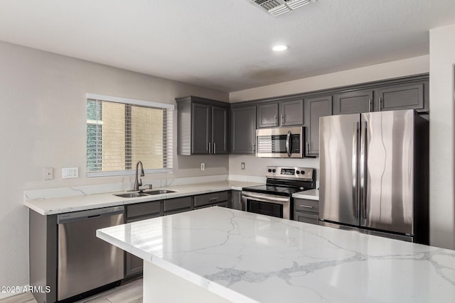 kitchen with light stone counters, visible vents, stainless steel appliances, and a sink