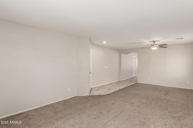 empty room featuring arched walkways, ceiling fan, carpet flooring, visible vents, and baseboards