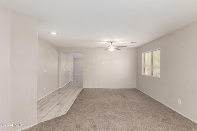 empty room featuring arched walkways, carpet flooring, visible vents, and a ceiling fan